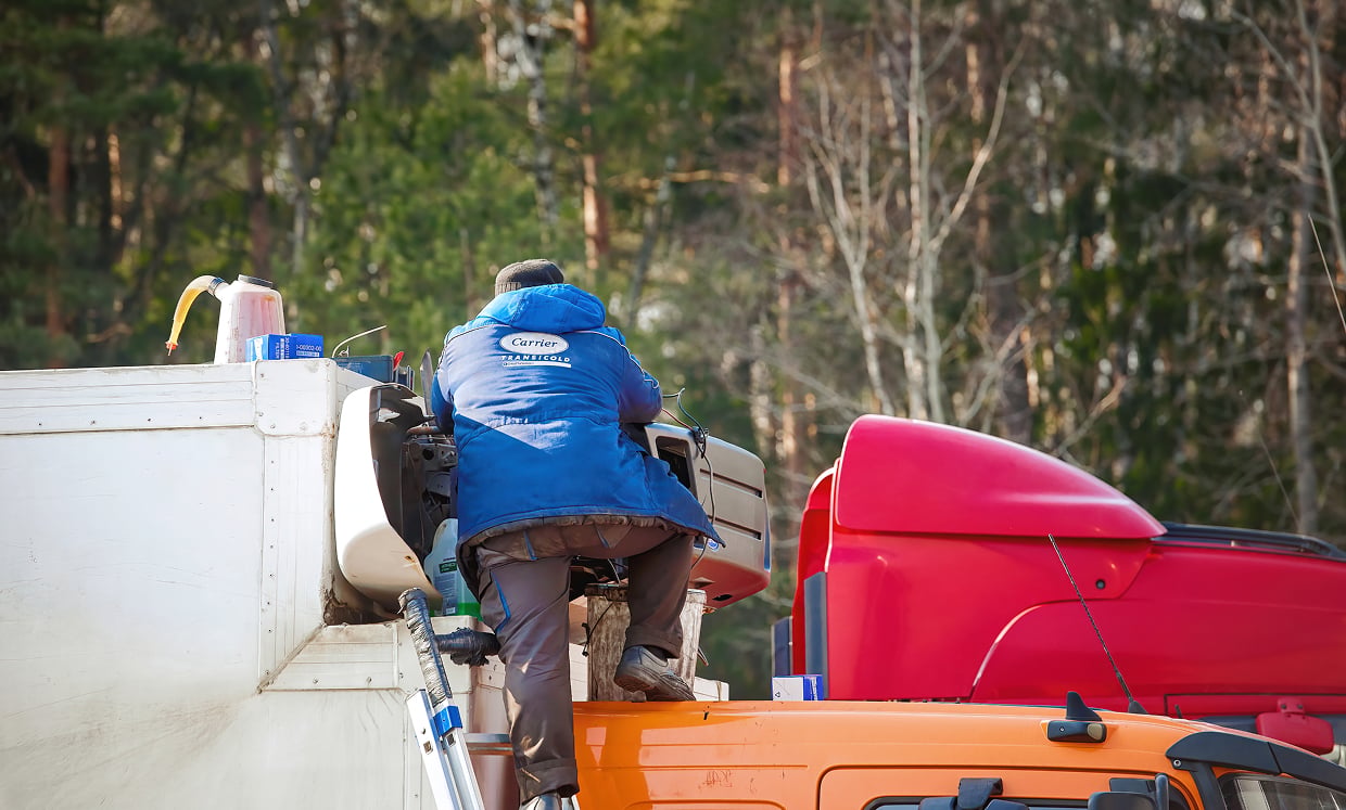 Helping Fleet Stay Road ready | Ares Diesel Repair worker in a blue jacket climbs into the cab of a white utility truck with an orange boat and red equipment nearby in a forested setting