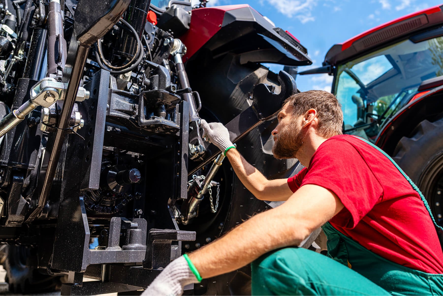 Technician in a Red Shirt and Green Overalls Inspecting a Large Industrial Machine with Exposed Hydraulics and Metal Components