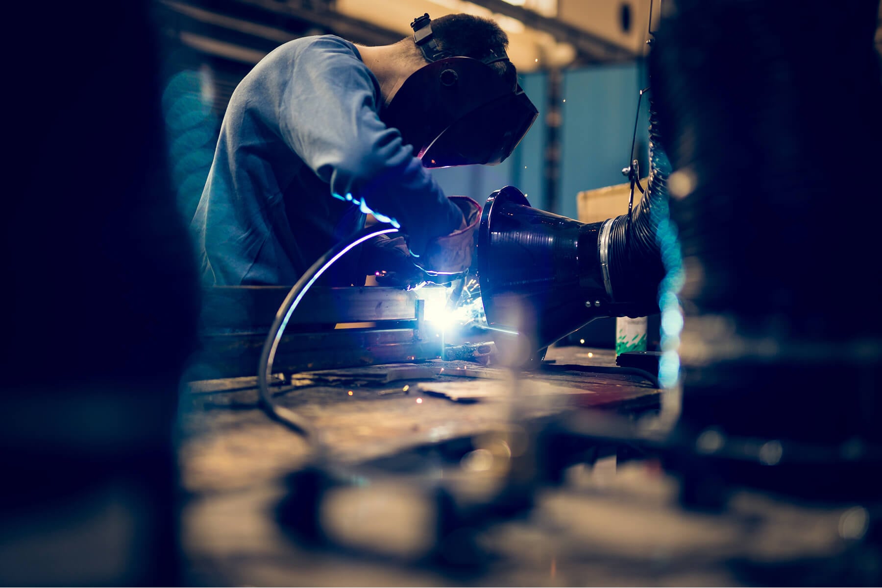 Welder Wearing a Helmet and Gloves Welding a Metal Joint with Bright Sparks in a Workshop