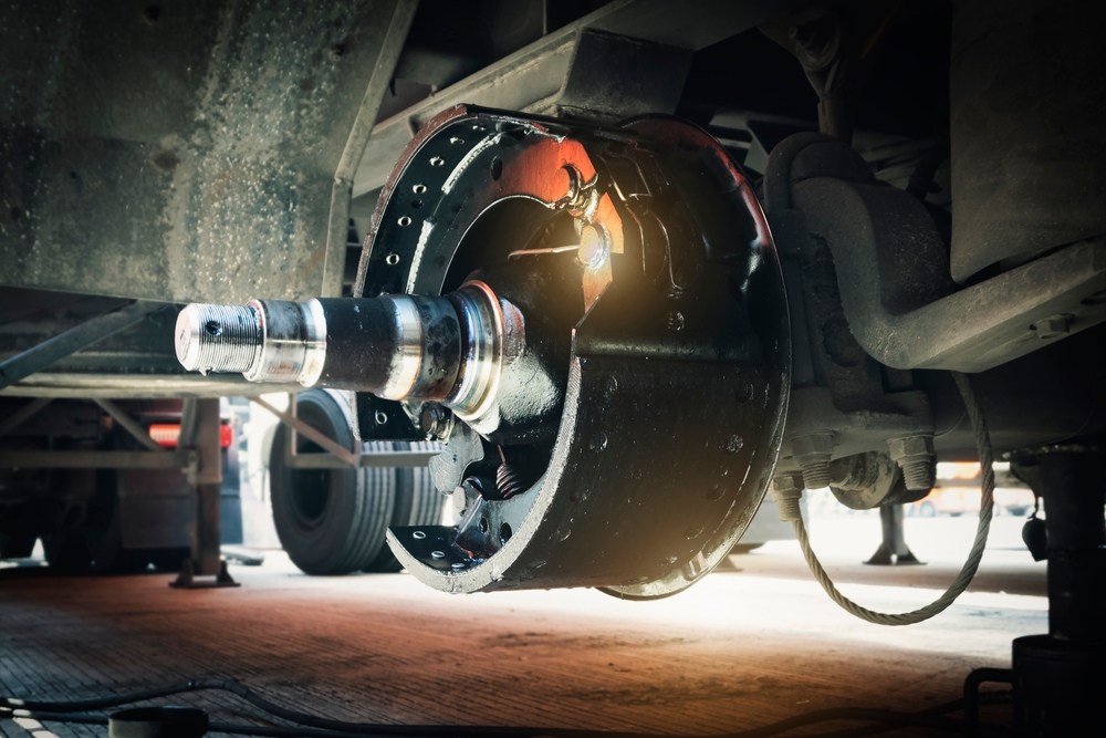 Close-up of a train wheel hub and axle with the brake drum removed, in a maintenance shed lighted by a warm glow