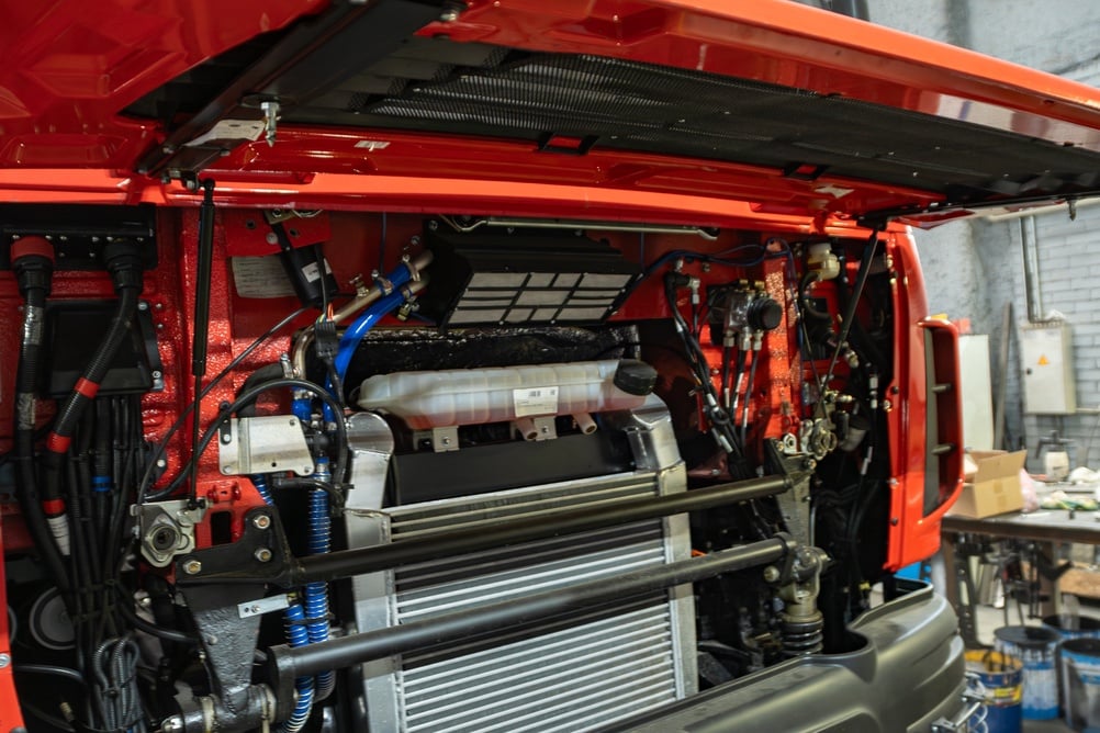 Red truck with hood up, exposing the engine and radiator components in a workshop.