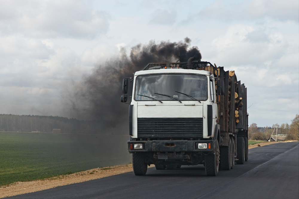 logging truck hauling a load of cut logs on a rural road thick black smoke trailing from the exhaust storming the sky